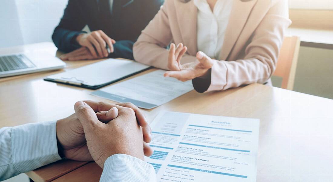 The perspective of an interview candidate as two people ask questions over a table with his CV.