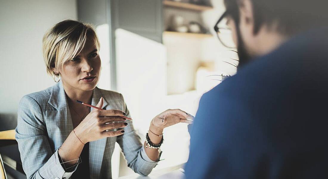 Side view of a man talking to his boss, a blonde woman wearing a white blazer.