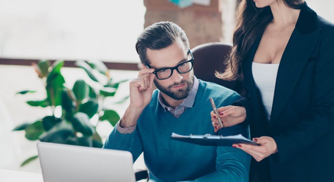 A man and a woman sitting opposite each other at a table in a well-lit office conducting an interview.