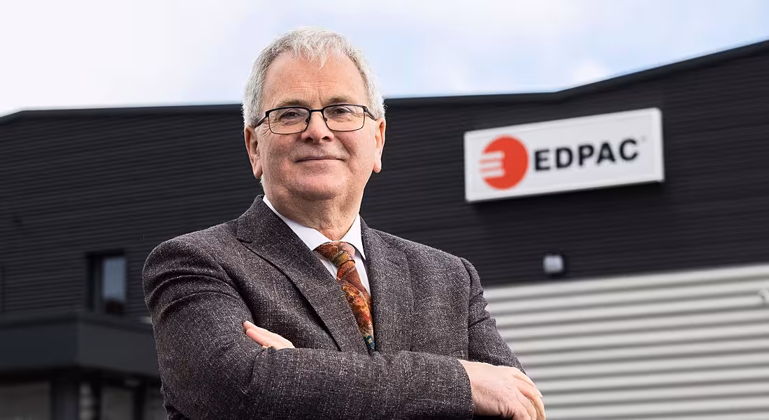 A grey-haired man with glasses wearing a suit stands outside an EDPAC facility.