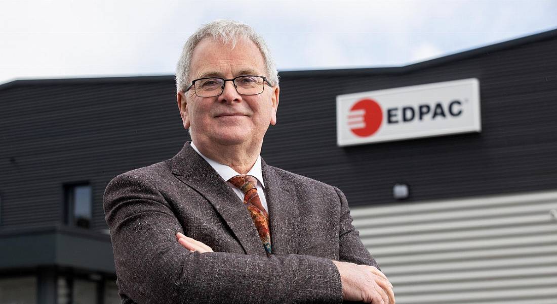 A grey-haired man with glasses wearing a suit stands outside an EDPAC facility.