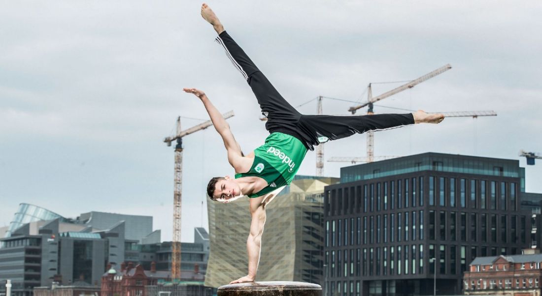 An Irish Olympian gymnast stands on one hand on a dock in Dublin's Silicon Docks.