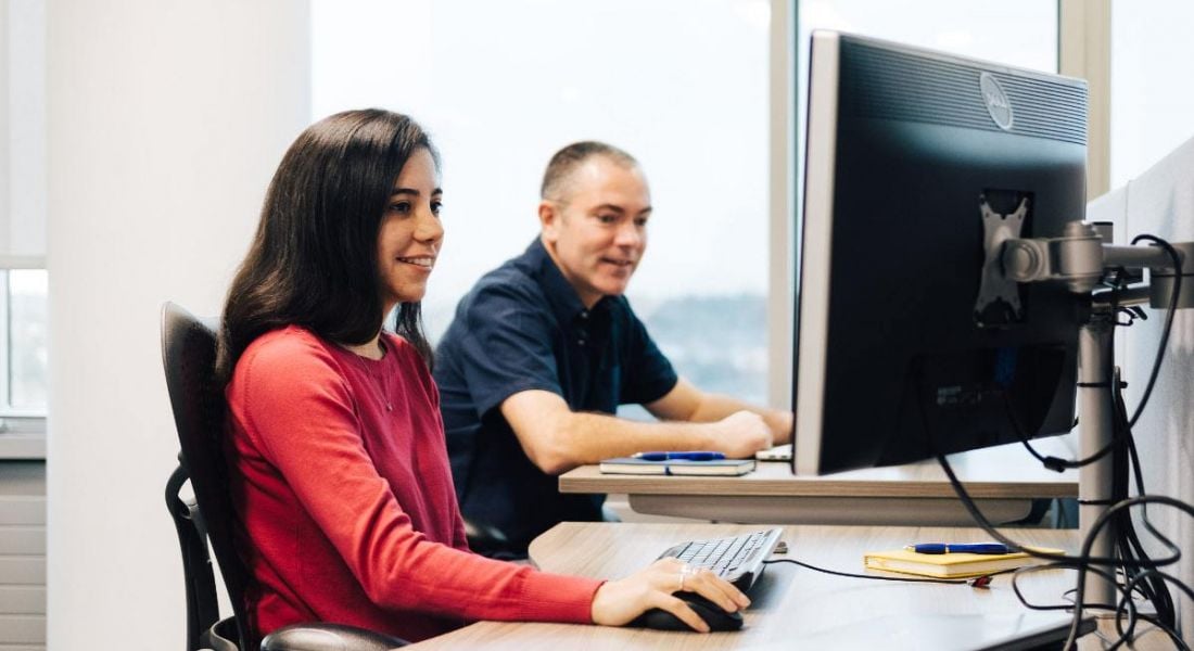 A female software engineer sits alongside a male software engineer at computers working.