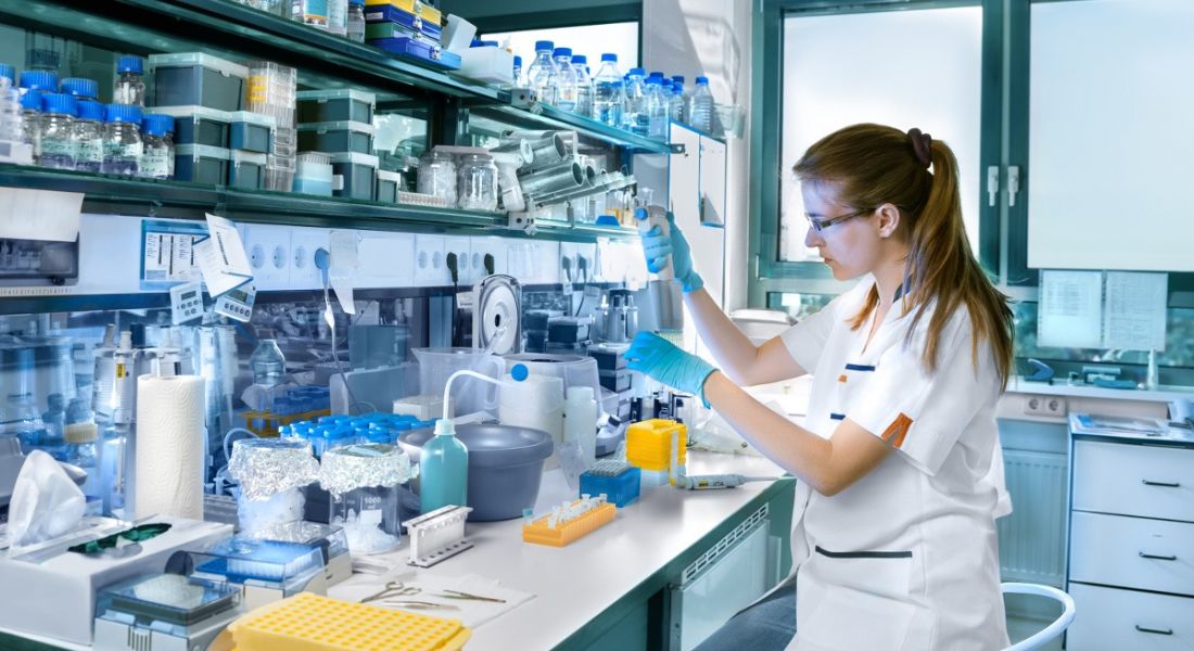 A young female scientist working in a lab surrounded by vials and equipment. She is showing off her life sciences skills.