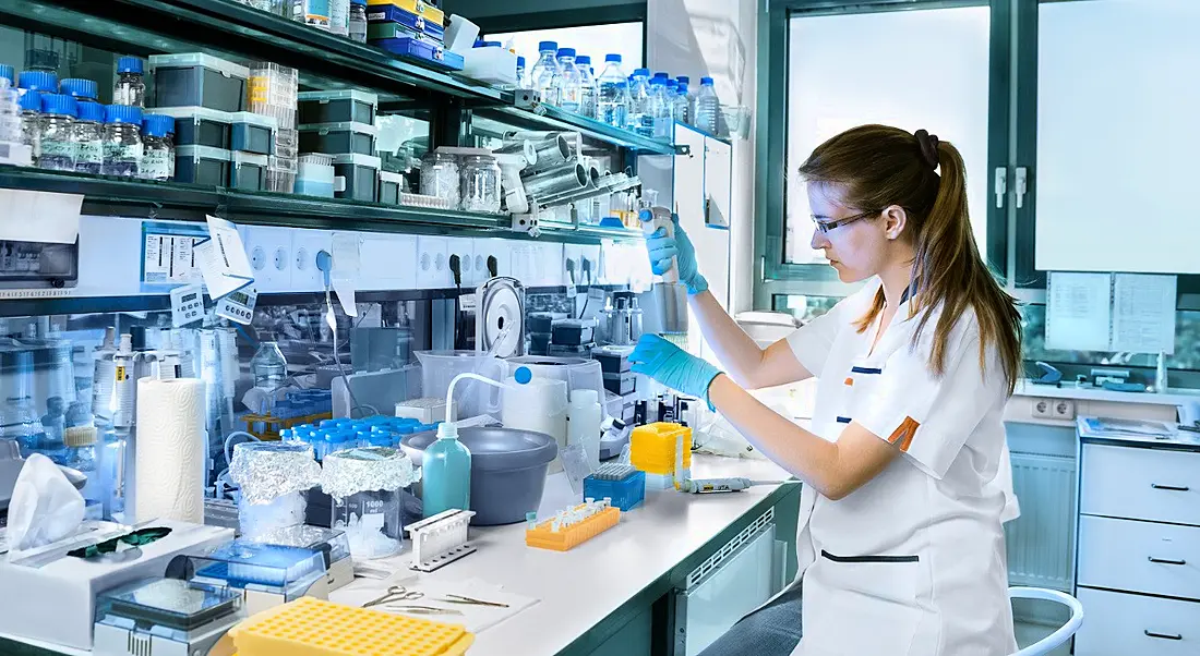 A young female scientist working in a lab surrounded by vials and equipment. She is showing off her life sciences skills.