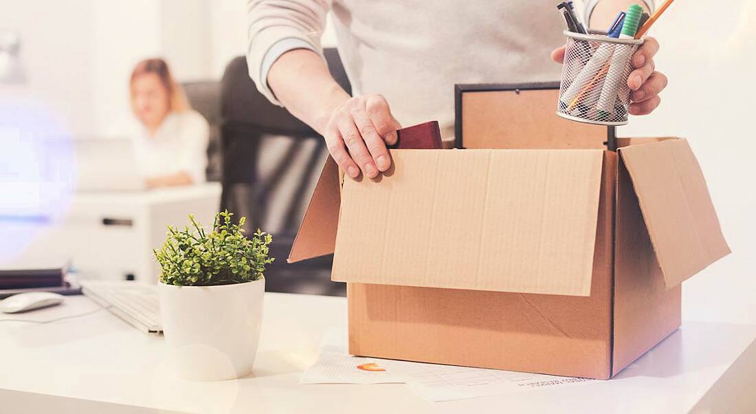 A close-up of an employee holding a box of their things from their desk because they have just quit their job.