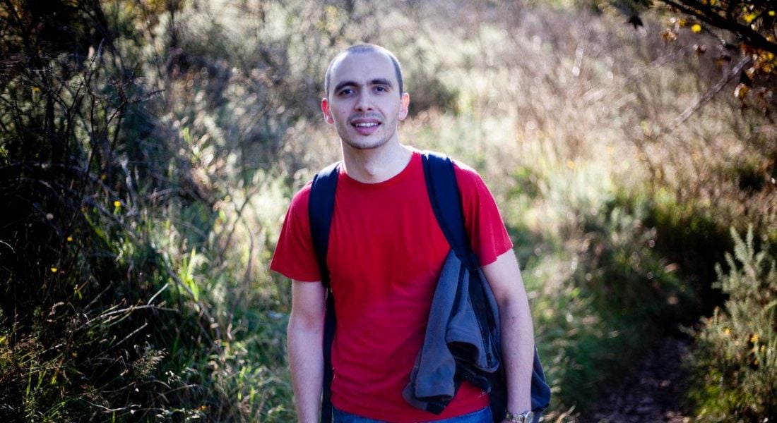 A young man in a red t-shirt standing outdoors in a woodland area. He works in Mastercard on a blockchain.