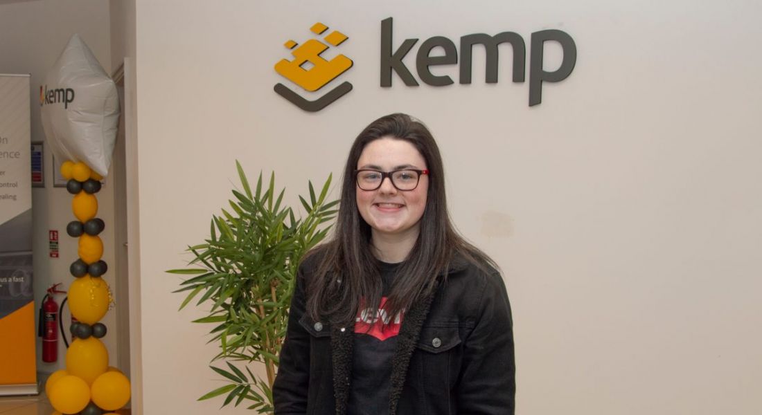 A young woman wearing a black jacket in front of the Kemp sign on a wall. She has completed an internship at the company.
