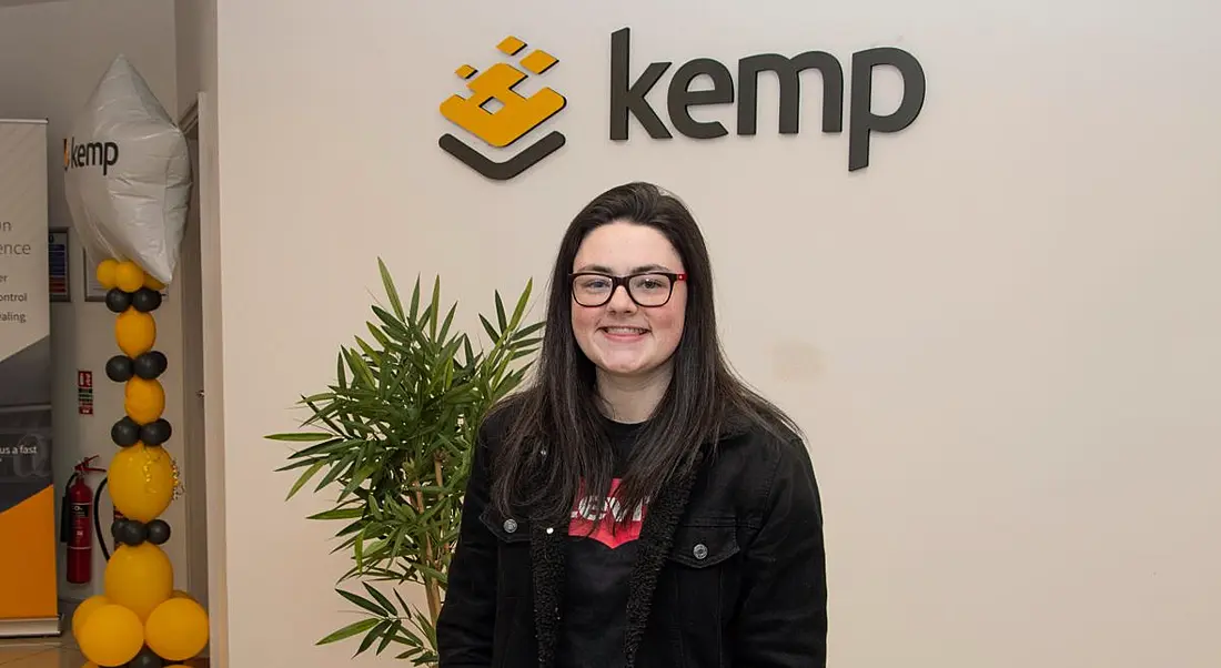 A young woman wearing a black jacket in front of the Kemp sign on a wall. She has completed an internship at the company.