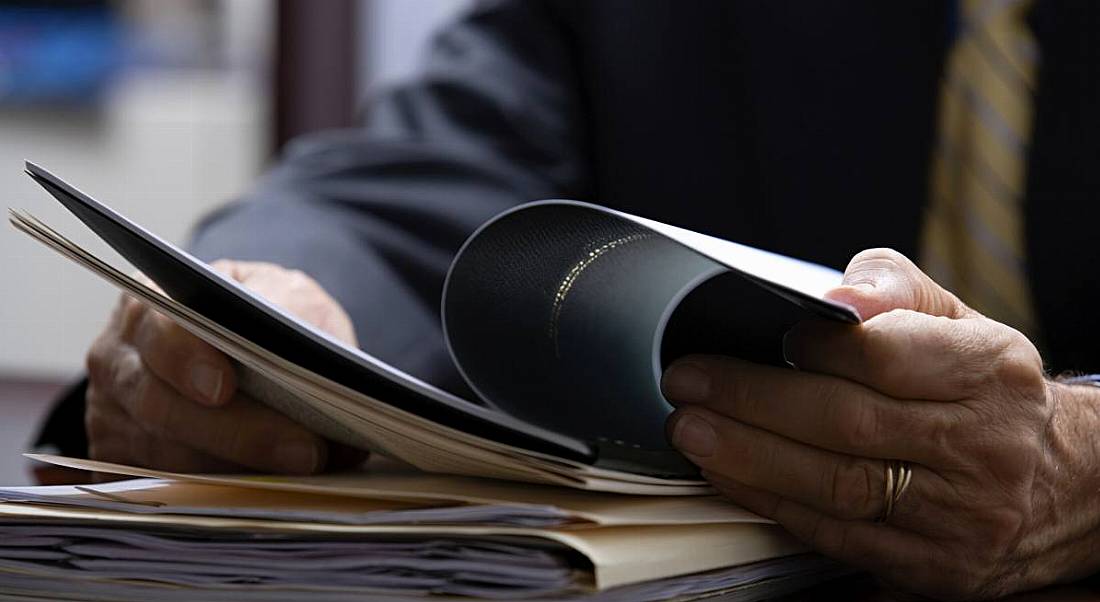 View of hands of a business man reading a reference amid a pile of job application paperwork.