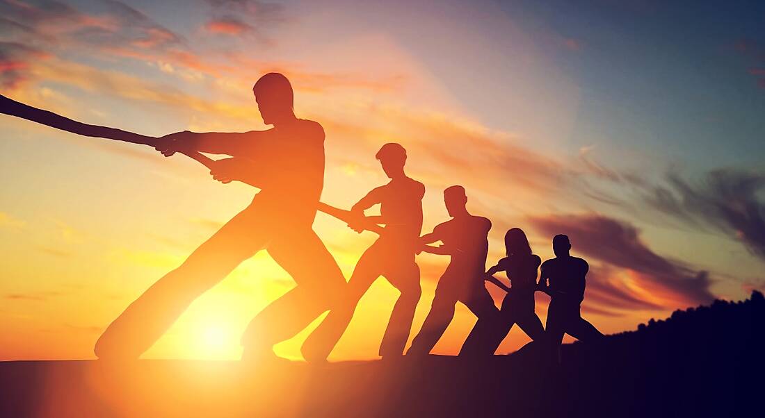 A silhouette of several people playing tug-o-war against a sunset. This depicts the financial industry battling for talent.