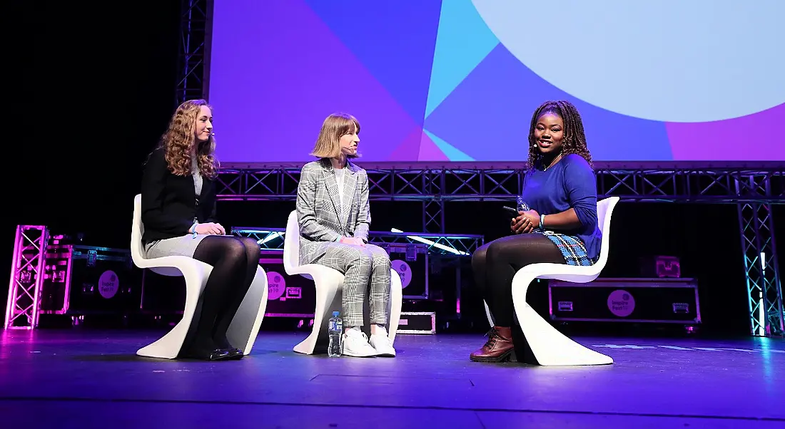 Three young women sitting in chairs on a stage at Inspirefest. They are discussing life for women in STEM.