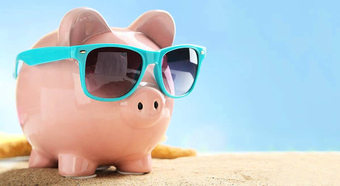 A pink piggy bank on a sandy beach in the sunshine with sunglasses. He is depicting hot jobs in fintech.