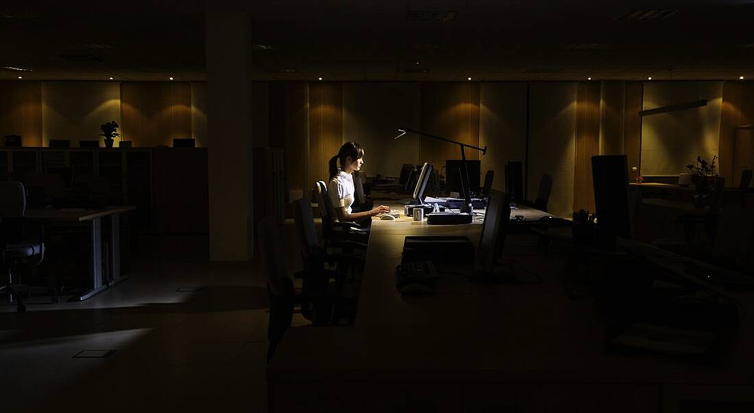 Side view of a young woman working on computer in dark office.