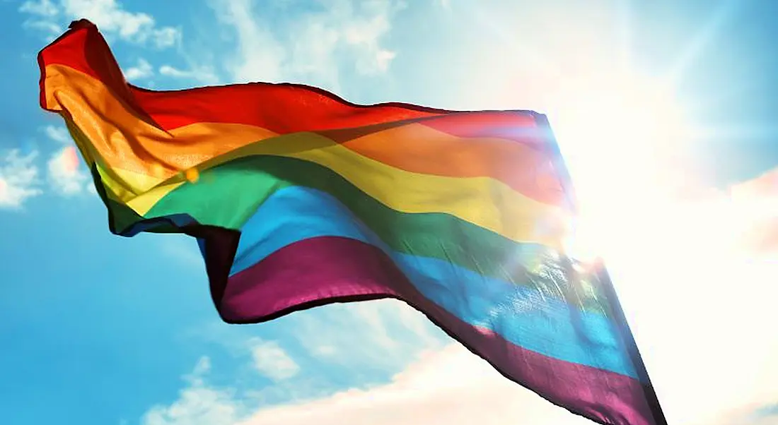 View of diaphanous rainbow Pride flag flowing in the wind on a blisteringly sunny day.