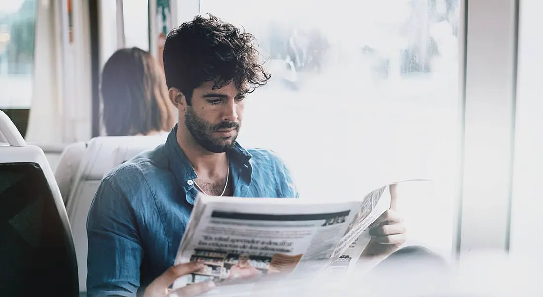 Man sitting next to window reading newspaper and looking for new job.