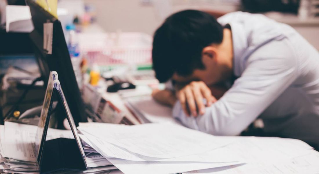 View of man at work with arms crossed on table and head bowed because he is stressed about his toxic work environment.