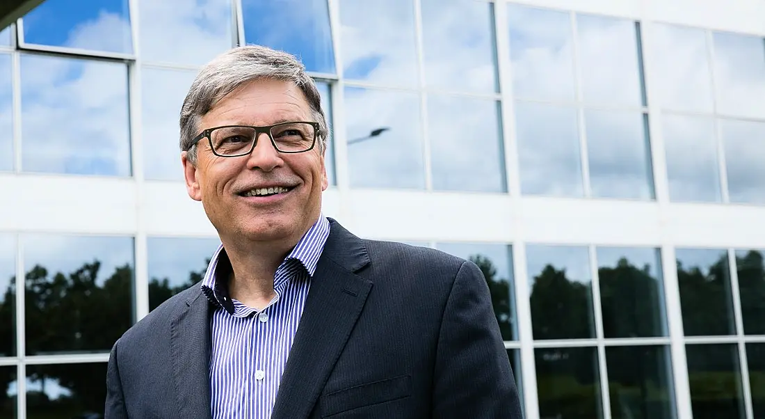 Esteemed looking business man looking to the distance and smiling wearing glasses and business suit in front of glass building.