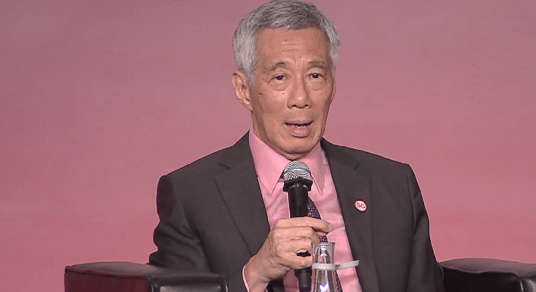 close-up of grey-haired man in pink shirt and dark suit jacket speaking into a microphone.