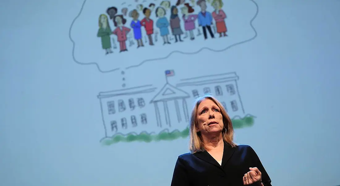 blonde middle aged woman in black speaking on stage in front of cartoon sketch of the White House with women in thought bubble above it.