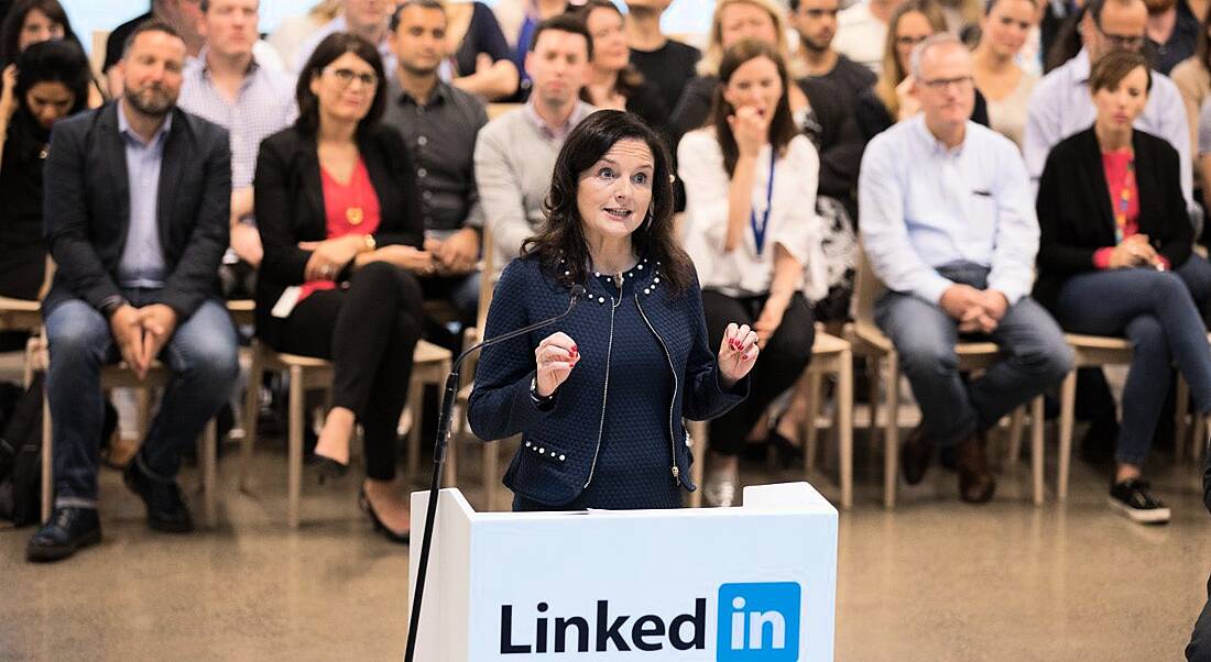 View of woman in navy professional business dress standing at LinkedIn platform announcing loads of jobs.