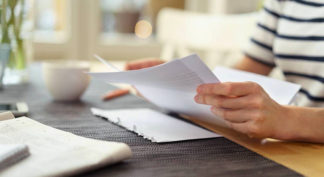 Close-up view of hands holding white paper on desk, reading over their cover letter.