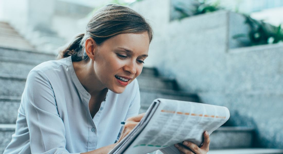 Young woman sitting on steps poring over newspaper on intrepid jobs search.