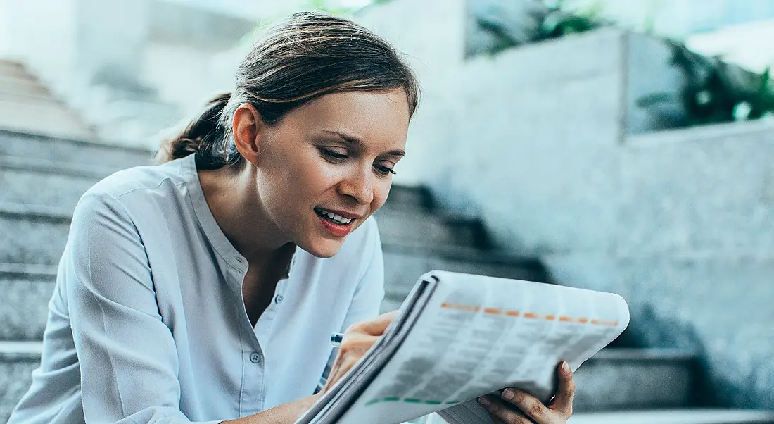 Young woman sitting on steps poring over newspaper on intrepid jobs search.