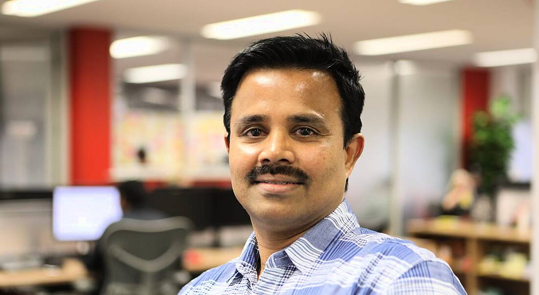 Image of a man in checked shirt with lustrious black mustache simpering at the camera.