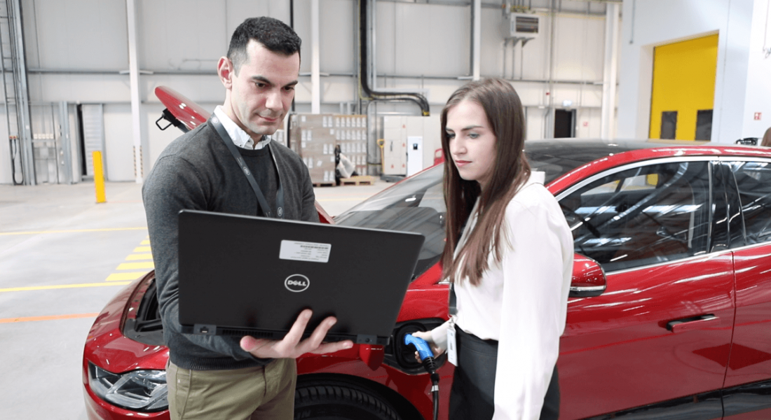 View of young male and female professionals looking at a laptop with a red car in the background.