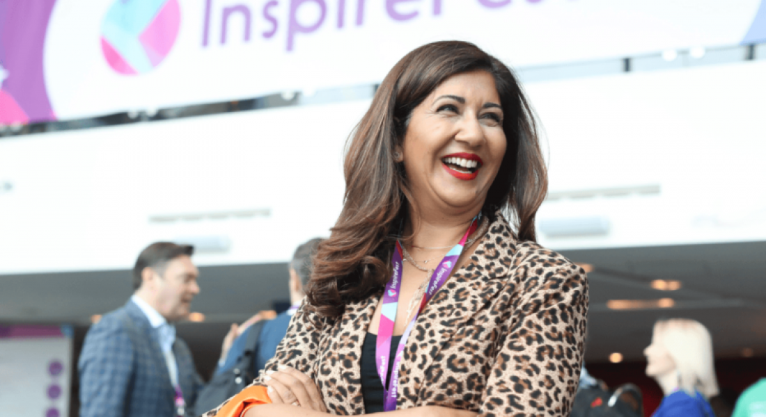 Nilofer Merchant stands in front of an Inspirefest sign, with dark hair and a leopard print suit on.