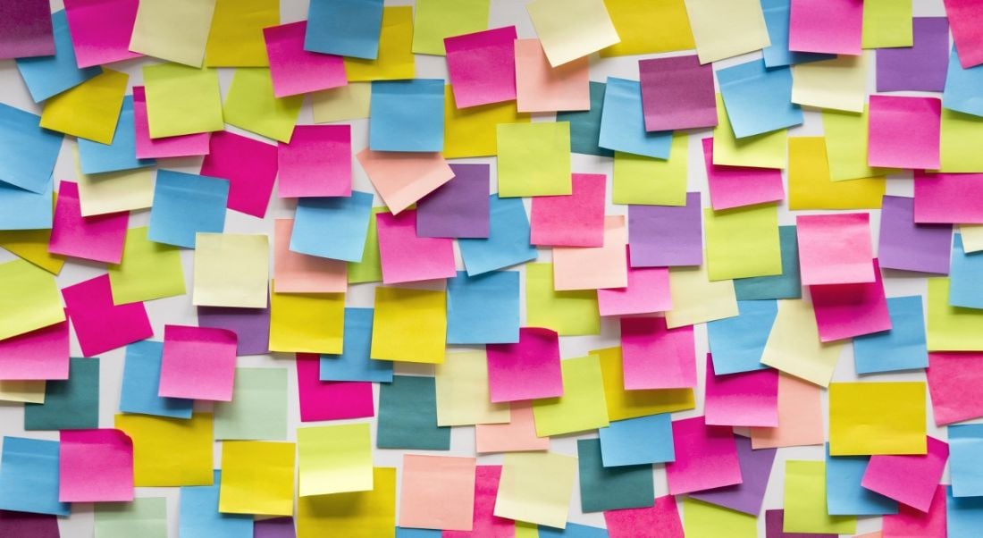 Multi-coloured sticky notes piled on top of each other on wall representing task debt concept.