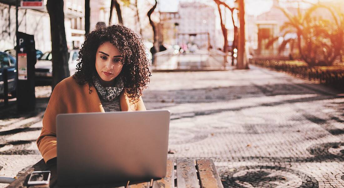 Young woman using her laptop outside on fall day swathed in scarf.