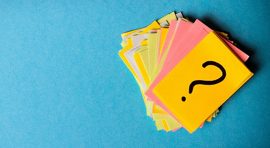 Stack of lurid coloured post-its with a question mark drawn on the top card, all sitting on a turquoise background.