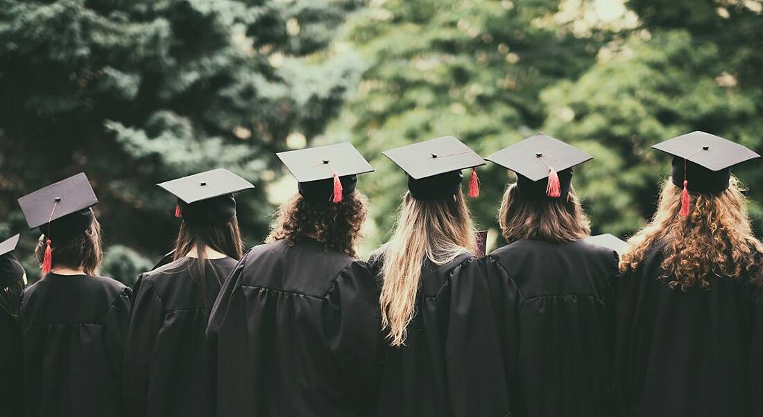 View of the back of a number of graduates celebrating in a verdant forest.