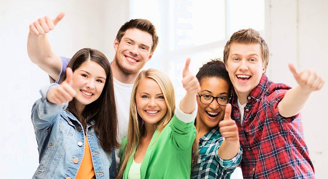 A group of young women and men in colourful clothing give a cheesy thumbs up to the camera.