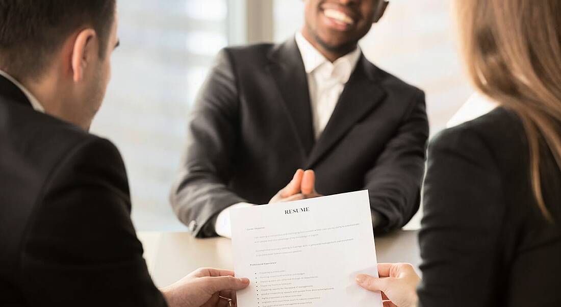 Employers review CV of confident job applicant smiling across table.