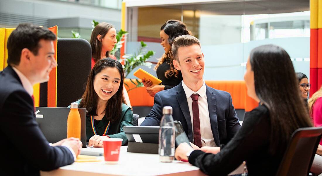 A group of young employees in business attire are sitting at a table and talking animatedly to each other.