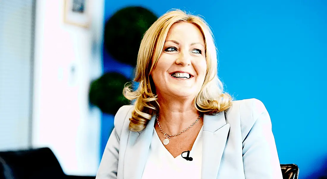 View of smiling blonde woman in light blue pant suit looking off camera in electric blue room.