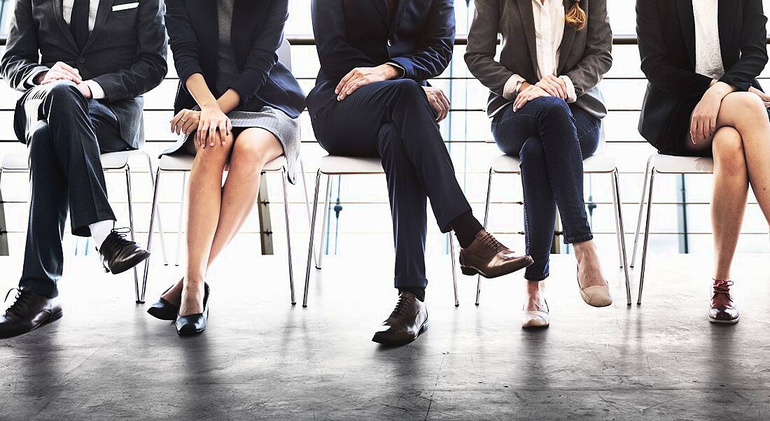 A row of men and women in business attire sitting down in a line side by side, only showing from the waist down.