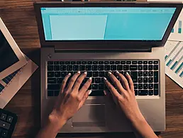 Robot sitting at a table and drinking coffee while working on a computer.