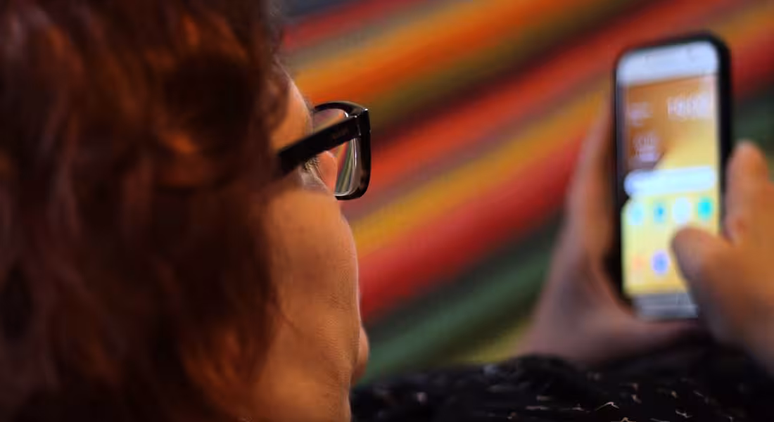Looking over the shoulder of a bespectacled woman as she plays a game on her smartphone.
