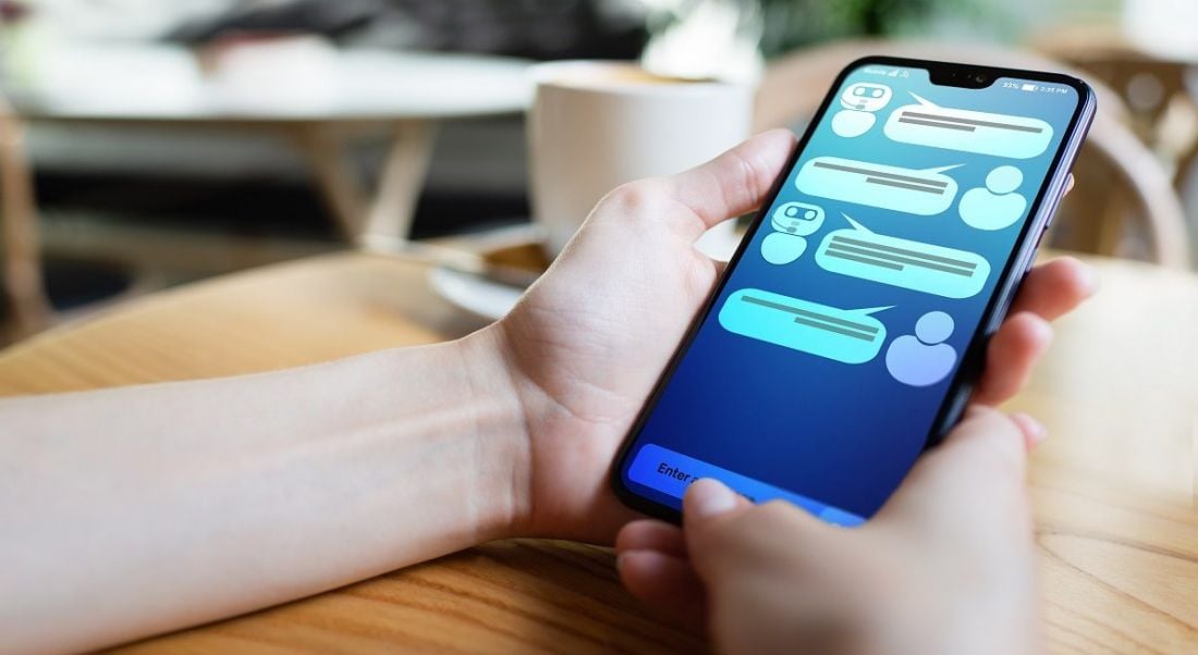 Person holding a mobile phone on a wooden table engaging with a chatbot.