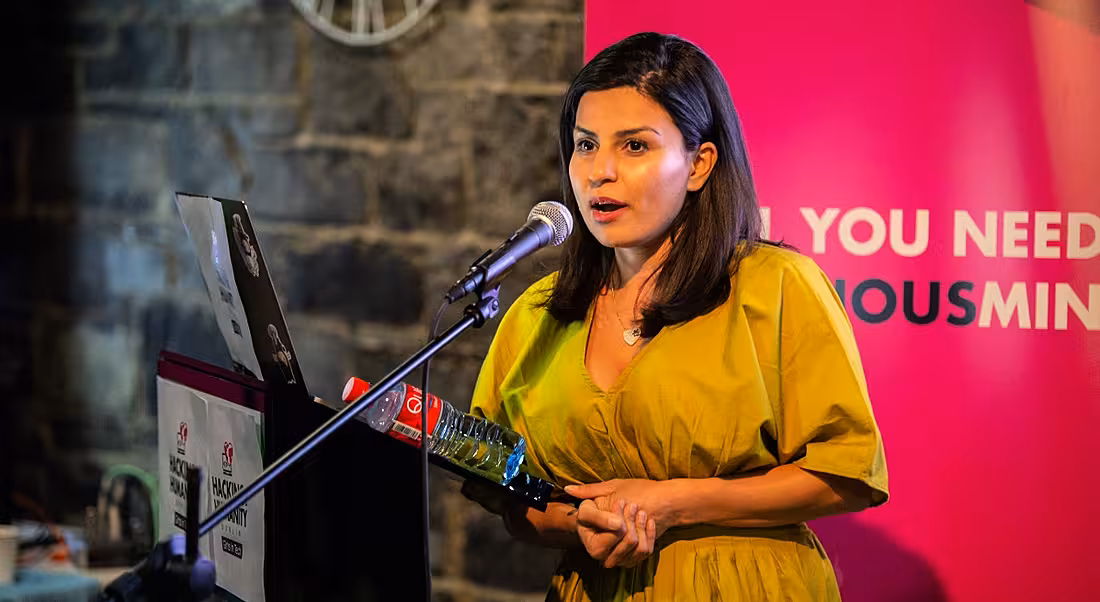 A woman in a bright dress is speaking into a microphone on an event stage