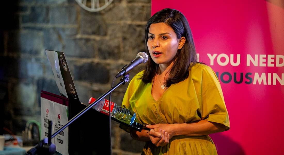 A woman in a bright dress is speaking into a microphone on an event stage