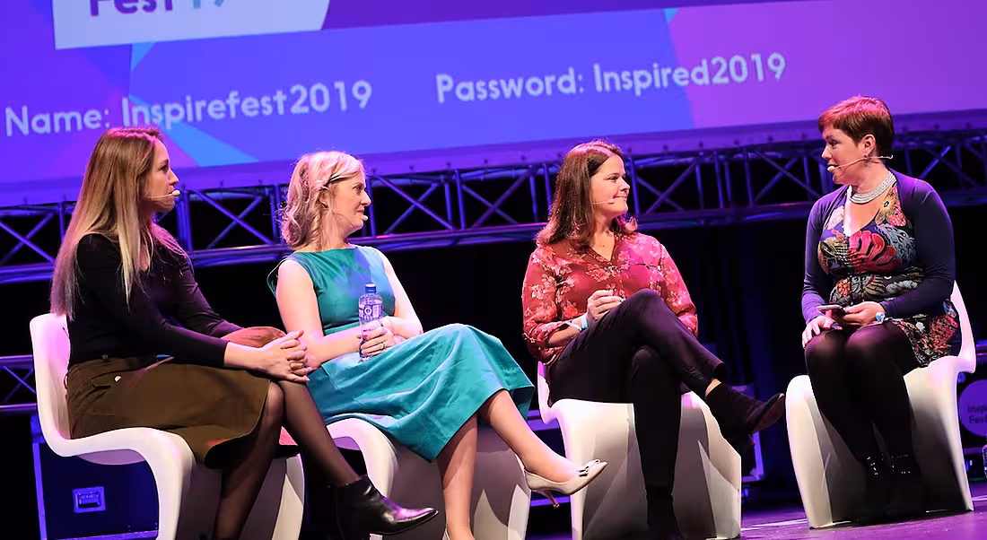 Four women are sitting on a stage and talking to each other.
