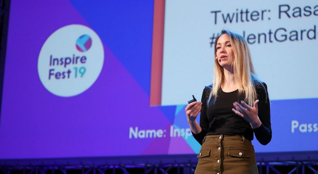 A woman giving a keynote speech is talking to the audience, standing on a stage.