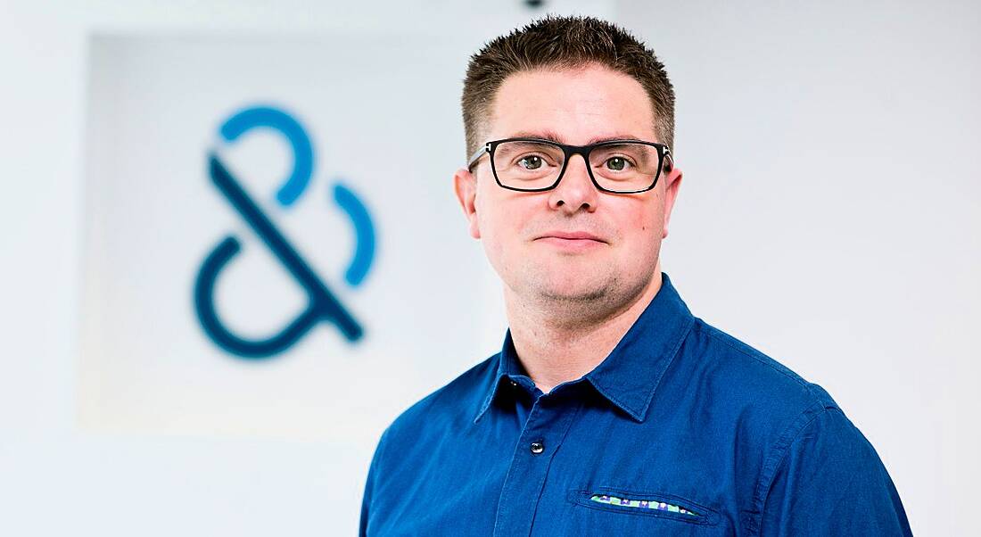 Corporate headshot of a man with glasses and a blue shirt in an office.