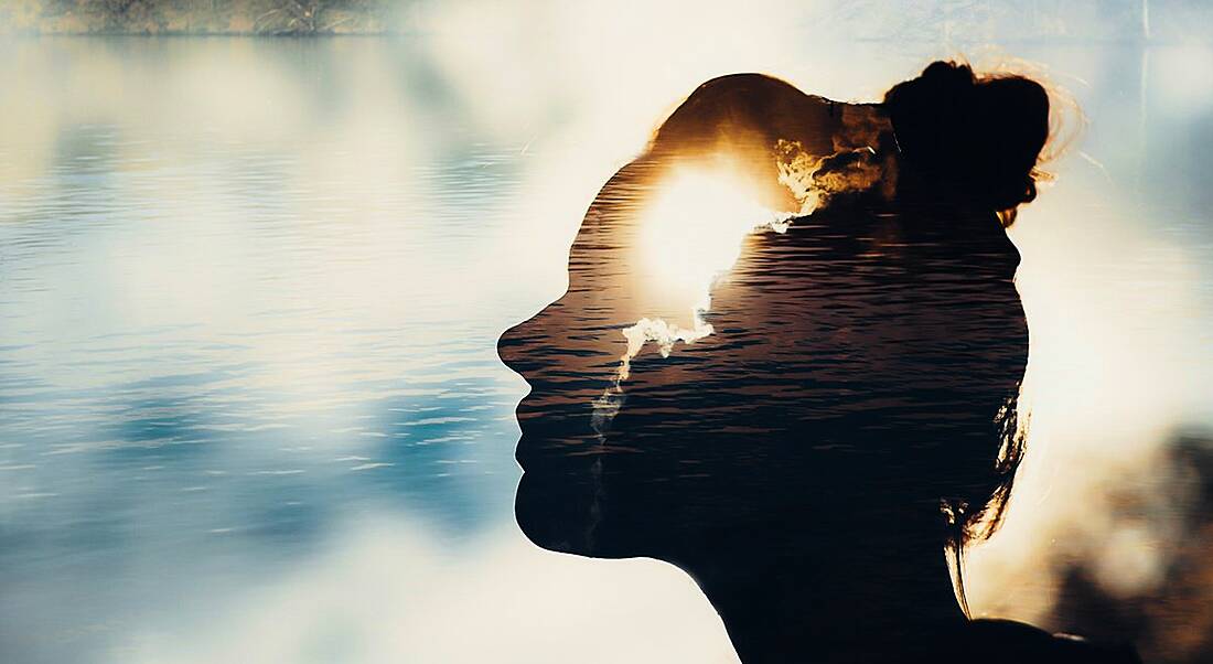 Abstract picture of a female silhouette with the sun shining through her head and a bright, cloudy sky in the background.