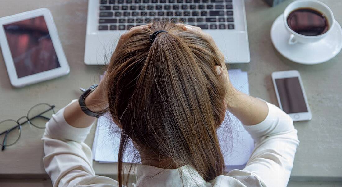 Top-down view of a businesswoman leaning on her work desk with her head in her hands.